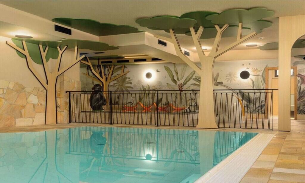 Une piscine intérieure avec un plafond décoré de motifs d’arbres et un mur en pierre.