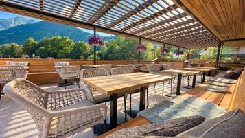 An outdoor seating area with wicker furniture, wooden tables, and a view of mountains.
