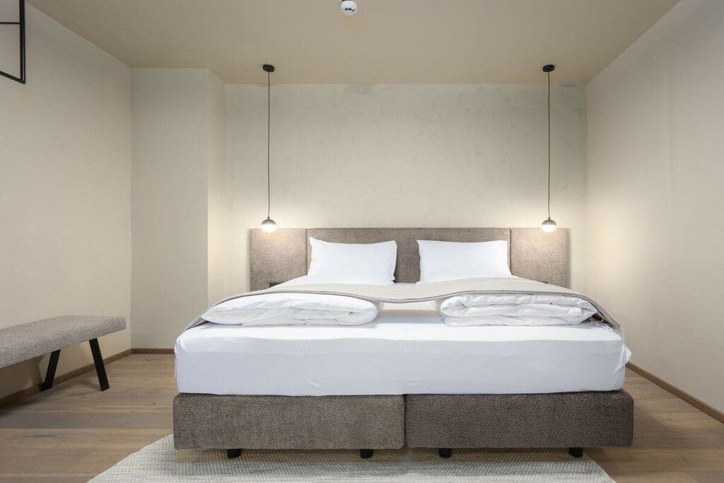 Une chambre à coucher moderne avec un lit, un banc et un luminaire suspendu.