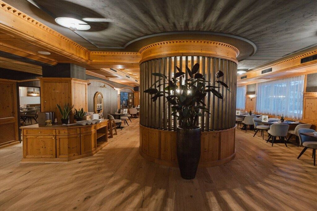 Un hall d’entrée spacieux avec une colonne centrale en bois, des coins salon et une grande plante en pot.