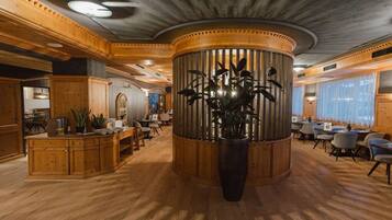Un hall d’entrée spacieux avec une colonne centrale en bois, des coins salon et une grande plante en pot.