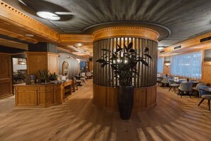 A spacious lobby with a central wooden column, seating areas, and a large potted plant. - Family apartment for 4 people (Kaprun)
