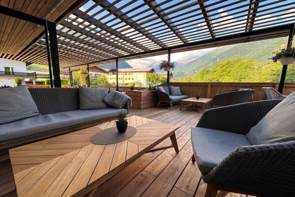 Un espace extérieur aménagé avec une terrasse en bois, un canapé et des fauteuils, offrant une vue sur un paysage montagneux.