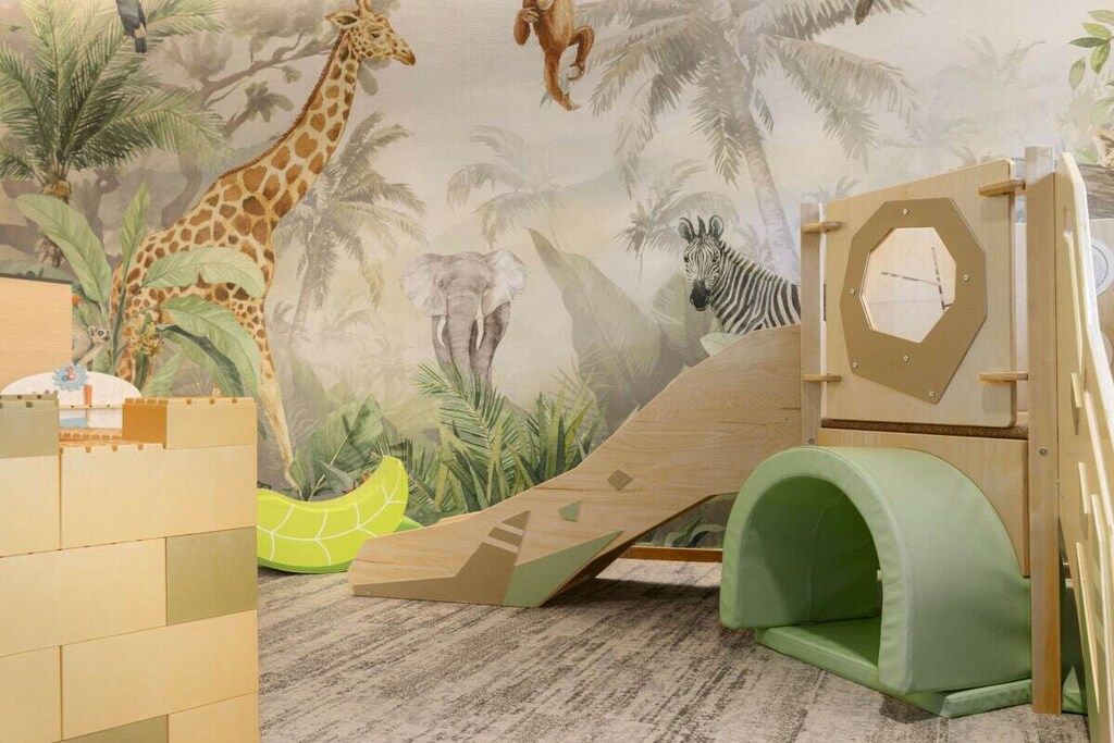 Un espace de jeux pour enfants avec une fresque murale, un toboggan et une structure d’escalade.