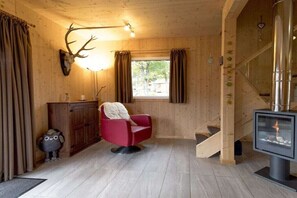 A wooden interior with a red chair, a deer head mounted on the wall, a fireplace, and a window with curtains. - Cabin with 1 bedroom (St. Georgen am Kreischberg)