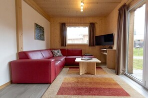 A modern living room with a red sofa, a wooden coffee table, a flat-screen TV, and a large window with curtains. - Cabin with 1 bedroom (St. Georgen am Kreischberg)