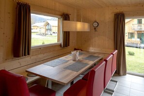 Ein Holzinterieur mit einem langen Tisch, roten Stühlen, einer Uhr und Blick auf Gebäude im Freien.