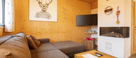 En hyggelig stue med en hjørnesofa, et fladskærms-tv, en pejs og et væghængt ur.