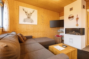 A cozy living room with a sectional sofa, a flat-screen TV, a fireplace, and a wall-mounted clock. - Cabin in Hohentauern with sauna (Hohentauern)