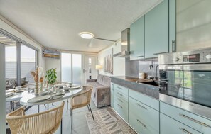 A modern kitchen with a built-in oven, a dining area with a round table and chairs, and a view through a large window.