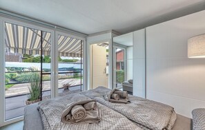 A modern bedroom with a large bed, a view of a balcony, and a mirror.