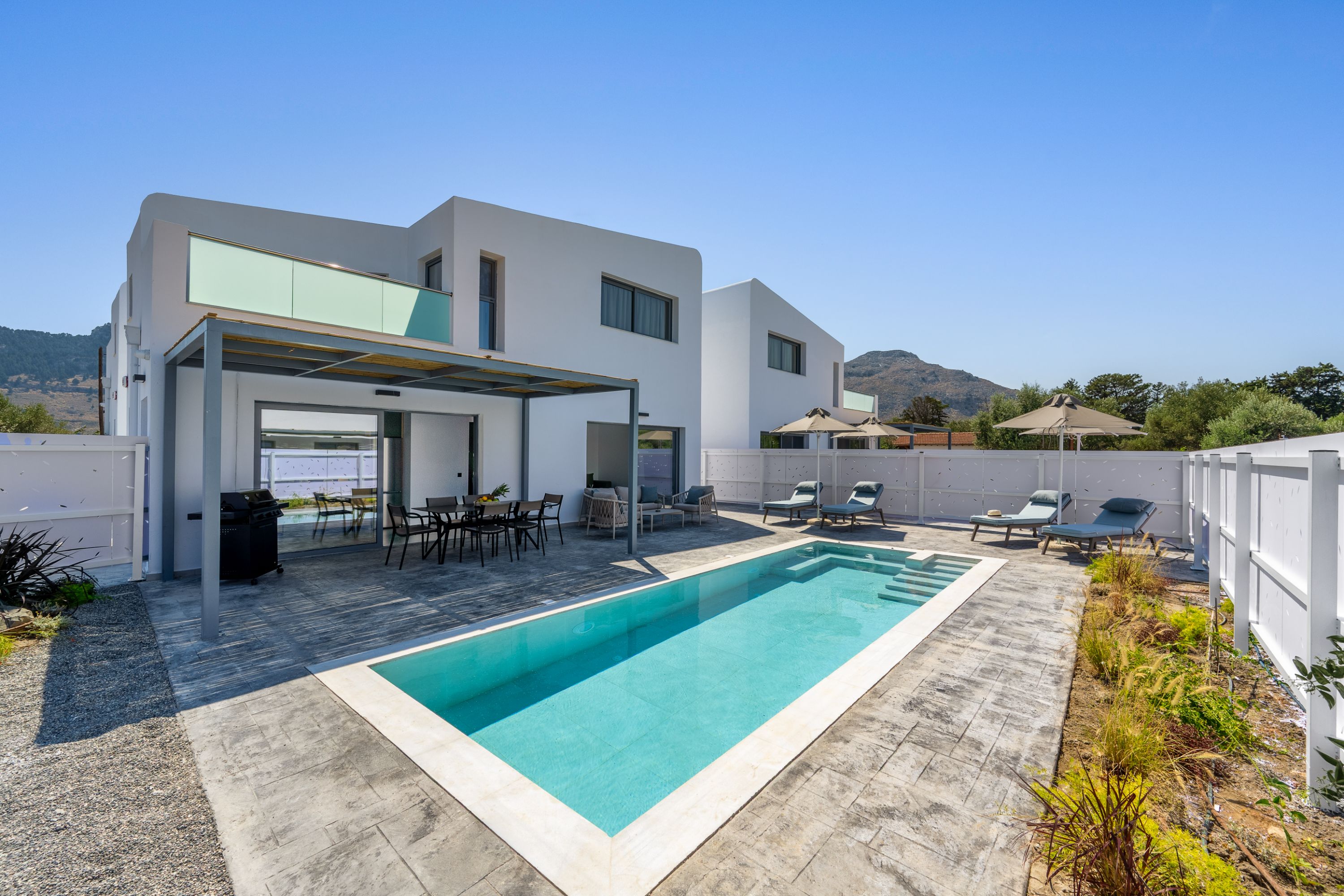 Une maison moderne à deux étages, dotée d’une piscine, d’un espace extérieur aménagé et offrant une vue sur les collines.