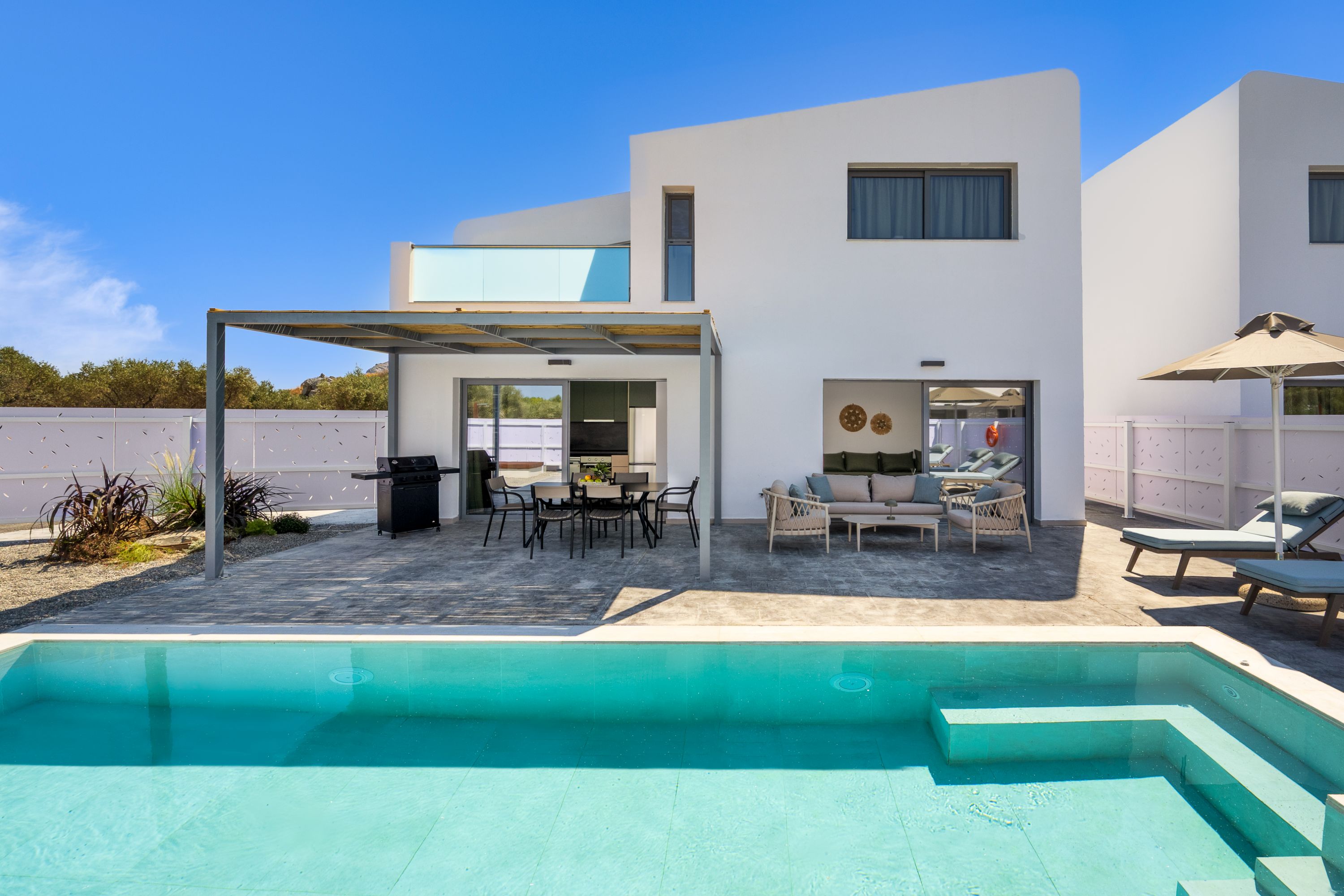Una casa moderna de dos pisos con piscina, mobiliario exterior y un patio cubierto.