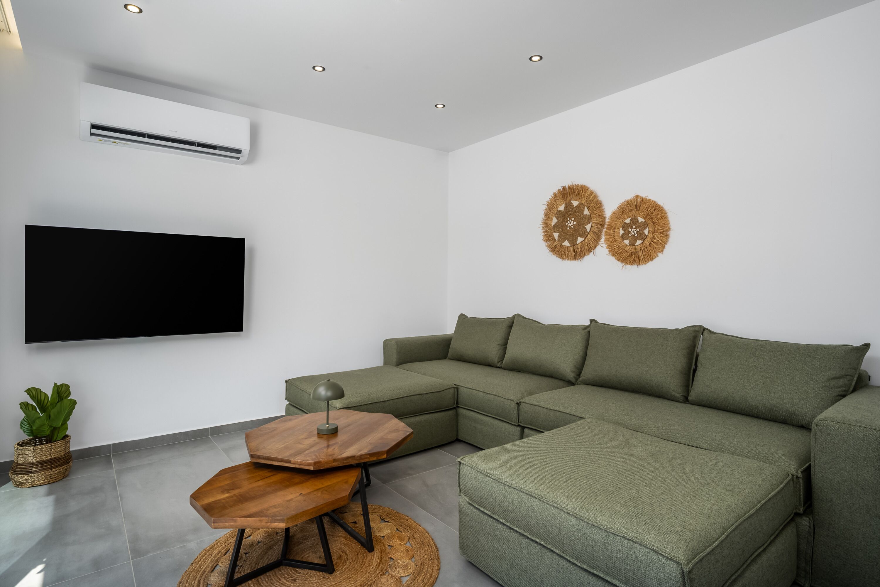 Een moderne woonkamer met een hoekbank, een flatscreen televisie, een klein houten tafeltje en twee decoratieve items aan de muur.