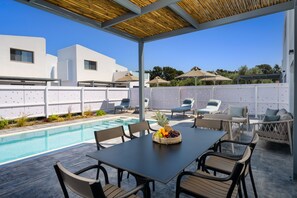 A poolside area with a table and chairs, a fruit basket, and a view of a modern building. - Villa located in Kolympia (Rhodes)