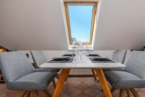 A dining area with a table set for four, two grey upholstered chairs, and a window above. - Störtebekerstraße 9 - Apartment 6 (Zingst (Ostseeheilbad))