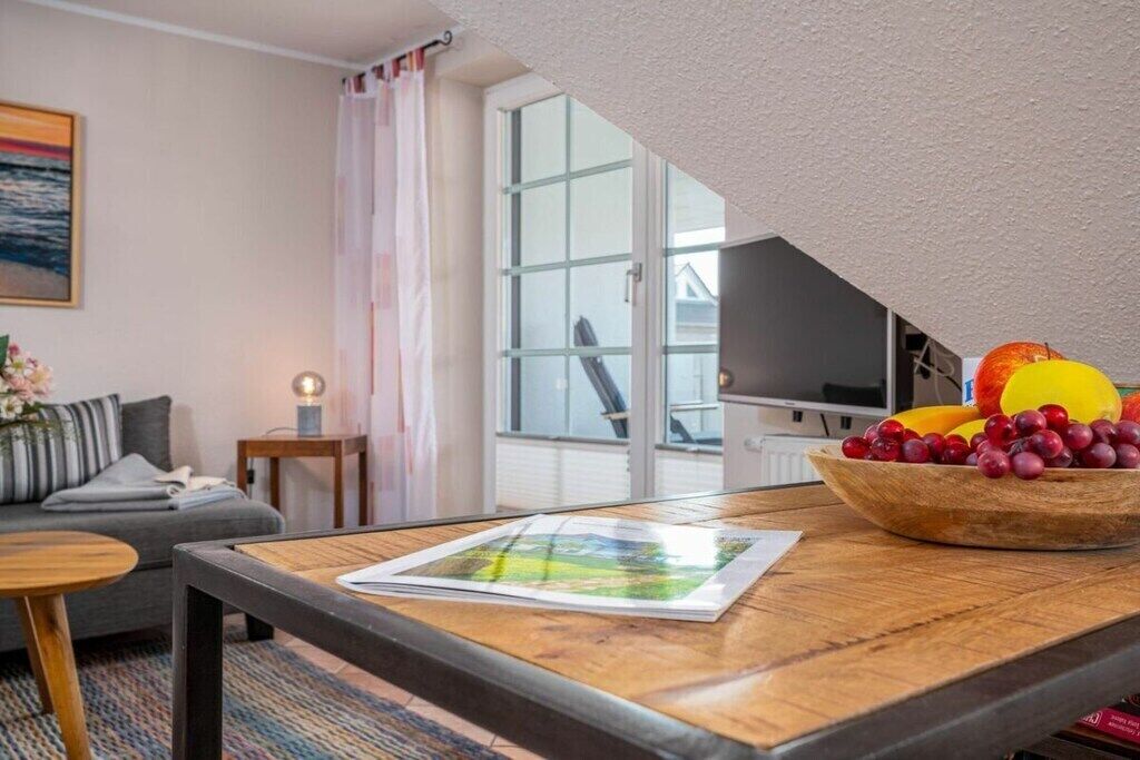 A modern living room with a sofa, a coffee table with a magazine, a fruit bowl, and a television.