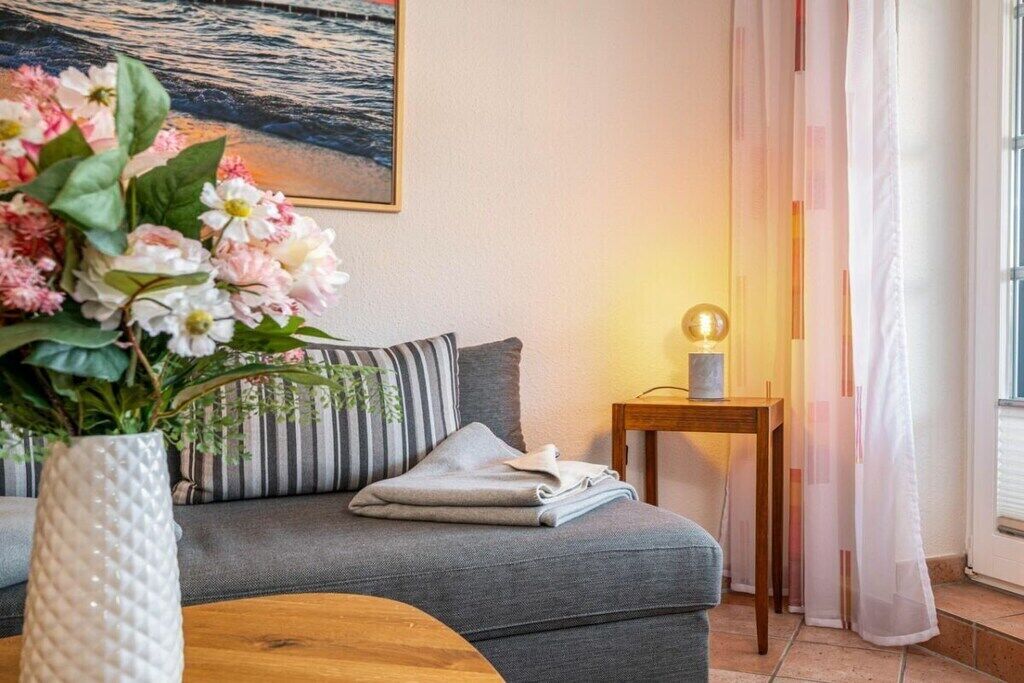 Un salon chaleureux avec un canapé gris, une petite table d’appoint en bois, un vase de fleurs et un tableau accroché au mur.