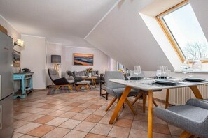 A dining area with a table set for four, a sofa, and a kitchen area with a refrigerator and a blue cabinet. - Störtebekerstraße 9 - Apartment 6 (Zingst (Ostseeheilbad))