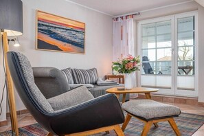 A modern living room with a sofa, armchair, and a small table with a vase of flowers. - Störtebekerstraße 9 - Apartment 6 (Zingst (Ostseeheilbad))