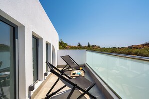 A balcony with two lounge chairs, a small table, and a glass railing overlooking a landscape with trees and hills. - Villa located in Kolympia (Rhodes)