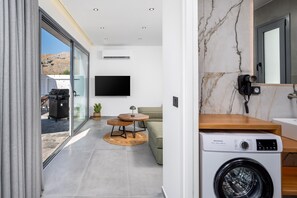 A modern living space with a washing machine, a flat-screen TV, and a dining area with a table and chairs. - Villa located in Kolympia (Rhodes)