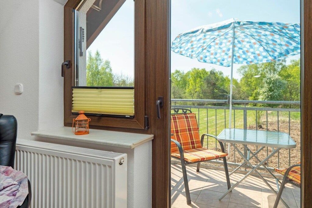 A room with a window, a radiator, a chair, a table, and an umbrella.