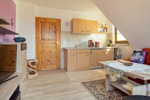 A kitchen with wooden cabinets, a dining table with a floral tablecloth, and a red sofa. - House Ahrens Apartment 5 (Zingst (Ostseeheilbad))