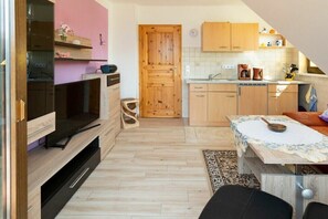 Een kleine keuken met houten kastjes, een inbouwoven en een eethoek met een tafel en stoelen.