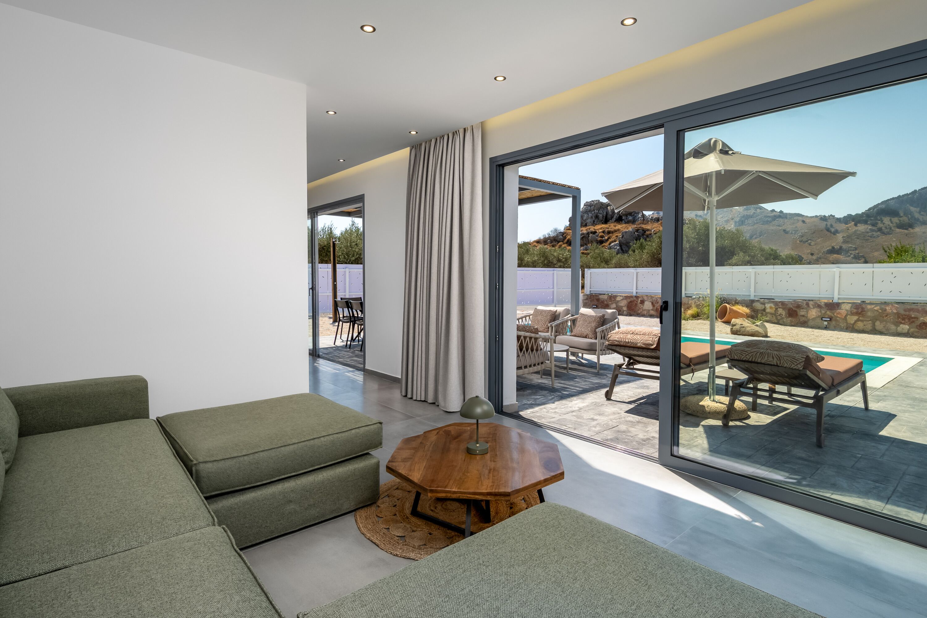 A modern living room with a sofa, a coffee table, and a view of an outdoor patio with a pool and seating area.