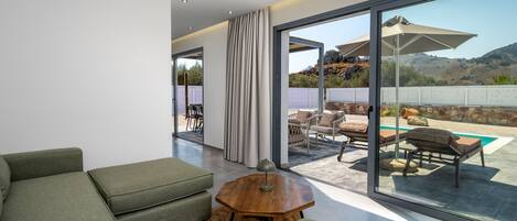 Un salon moderne avec un canapé, une table basse et une vue sur une terrasse extérieure dotée d’une piscine et d’un espace salon.