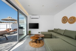 Een moderne woonruimte met een glazen wand, een flatscreen televisie, een groene bank en een klein houten tafeltje.