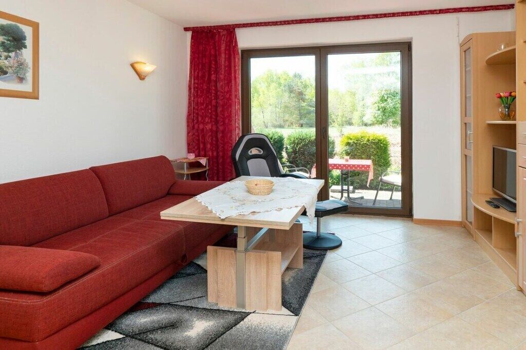 Un salon avec un canapé rouge, une petite table sur laquelle se trouve un panier, un fauteuil et un meuble pour la télévision.