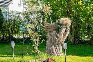 A tree stump with a woven basket and a microphone on top, surrounded by greenery and a house in the background. - Störtebekerstraße 9 - Apartment 5 (Zingst (Ostseeheilbad))