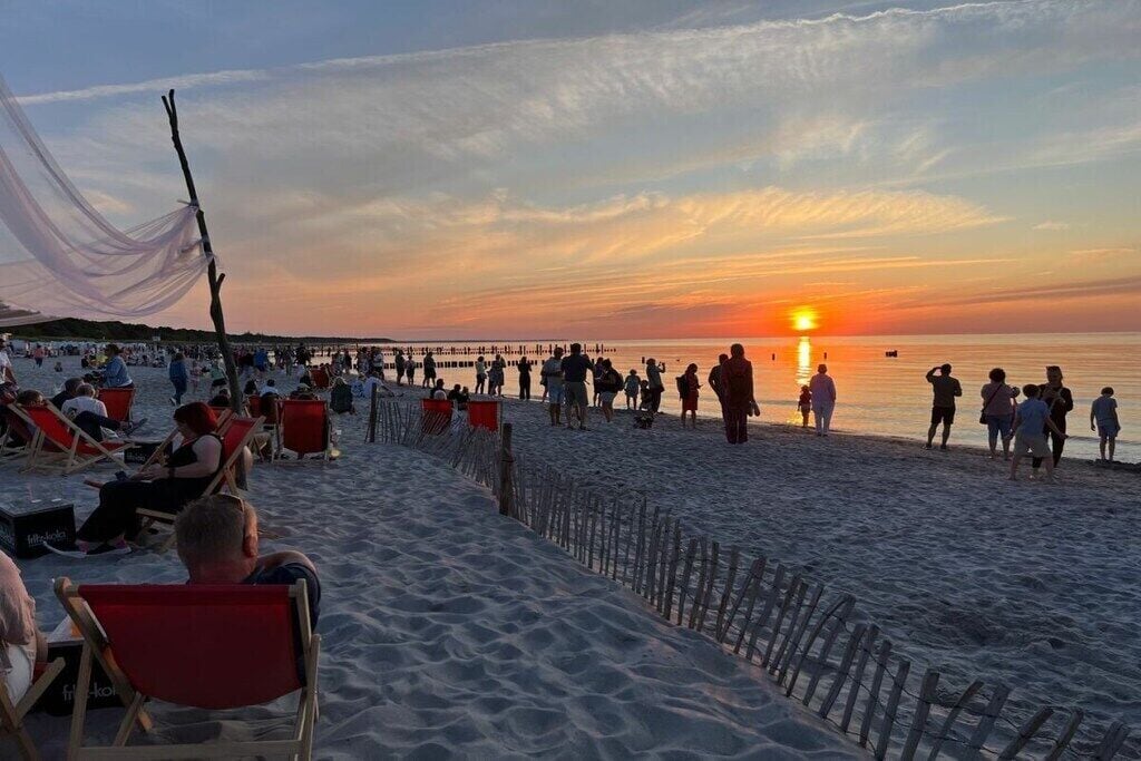 Praia com pessoas, cadeiras e um pôr do sol.