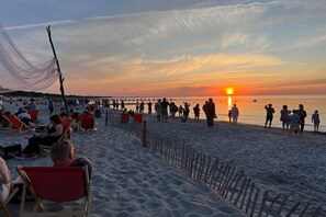 Une plage avec des gens, des chaises et un coucher de soleil.