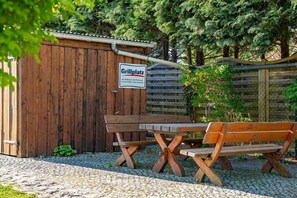 Un espace extérieur aménagé avec des sièges en bois, agrémenté d’un panneau indiquant « Grillplatz », ce qui signifie qu’il s’agit d’un espace barbecue.