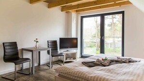 Une chambre à coucher comprenant un lit, un bureau, une chaise, un téléviseur et une fenêtre donnant sur des arbres.