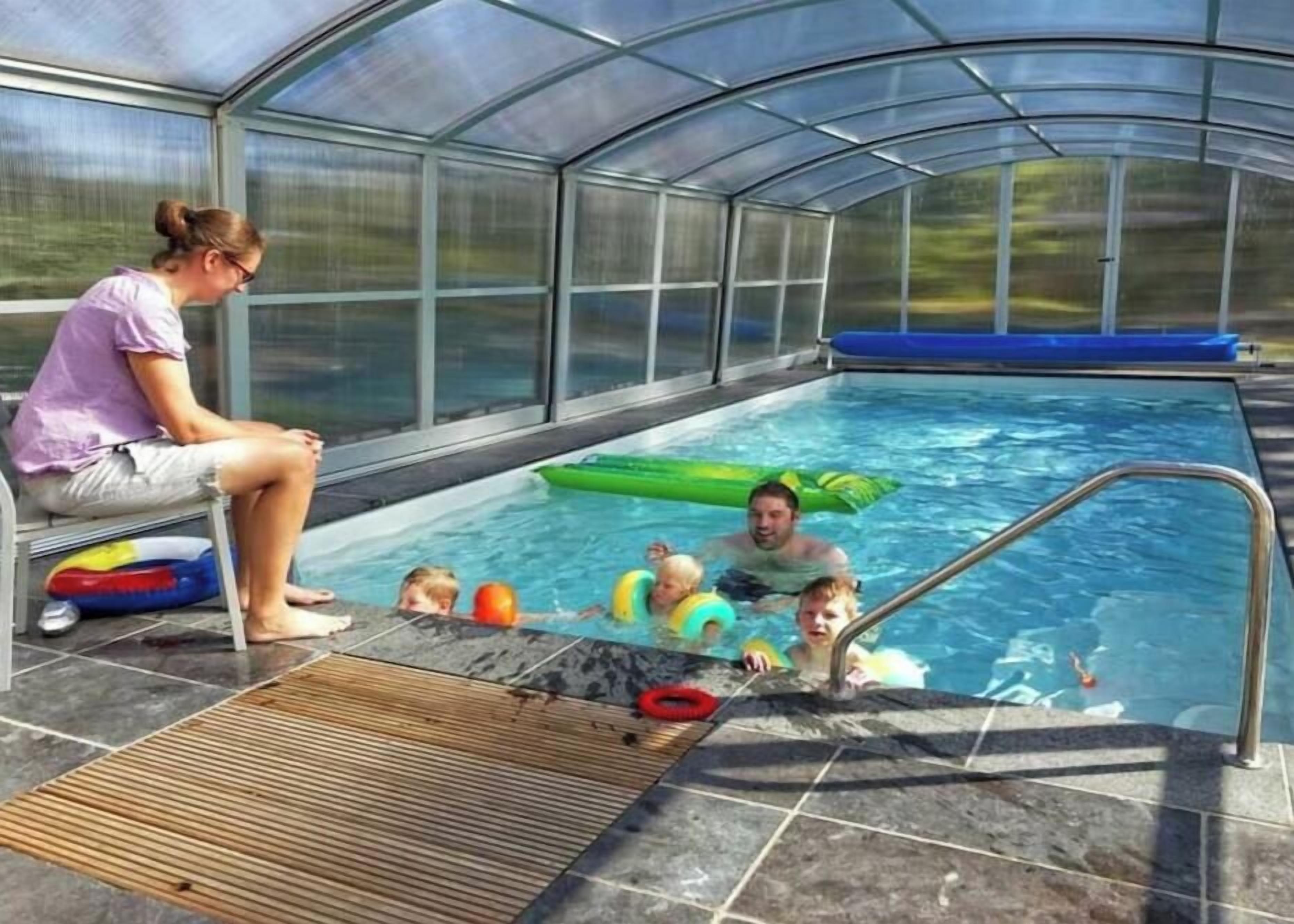 Zona de piscina amb tancament de vidre, un tauló de llançar i joguets inflables.