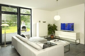 Una sala de estar moderna con un sofá blanco, un televisor de pantalla plana, una planta en maceta y una chimenea.