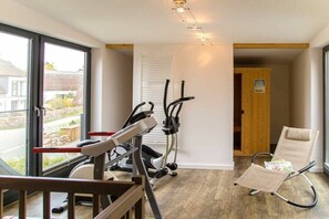 Ein Zimmer mit einem Ergometer, einem Rudergerät und einem Massagesessel.