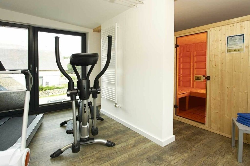 Ein Fitnessraum mit Laufband, Crosstrainer und einer Sauna, die durch eine Tür sichtbar ist.