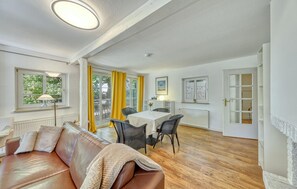 A room with a leather sofa, a dining table with chairs, a radiator, and a window with curtains. - 3 bedroom beautiful apartment in Krems II (Krems II)