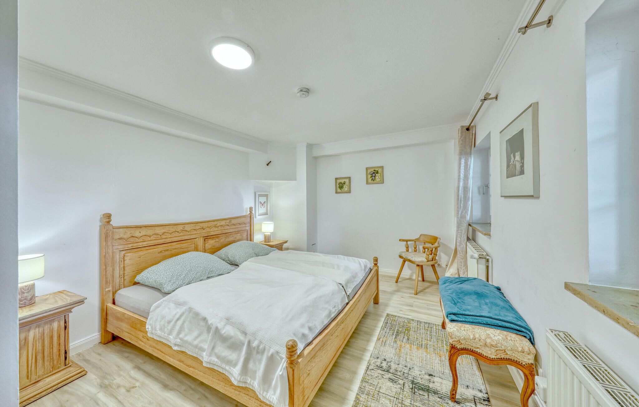 A bedroom with a wooden bed, a bedside table, a chair, and a radiator.