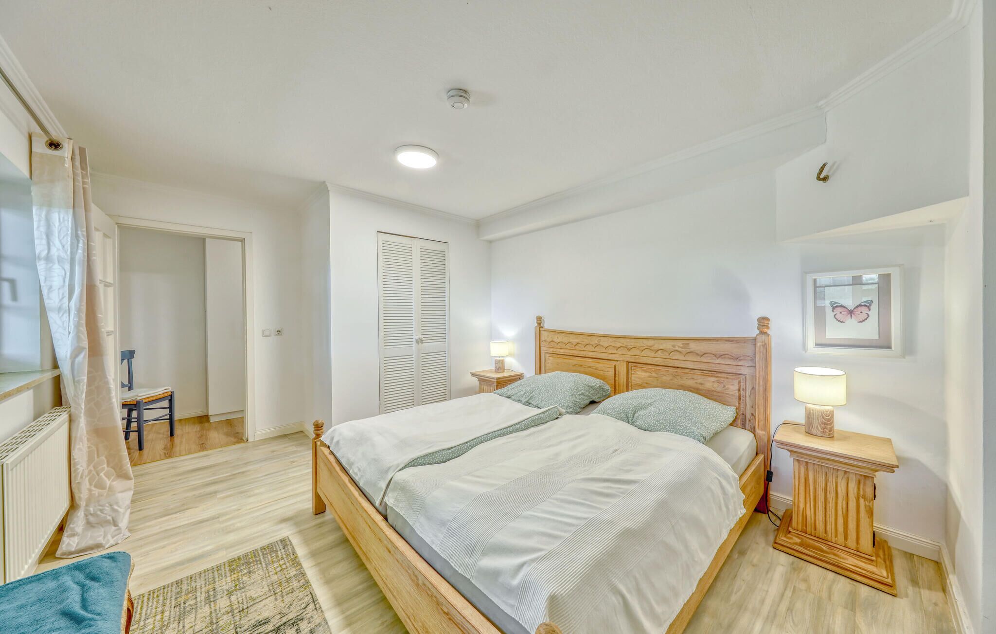 Ein Schlafzimmer mit einem hölzernen Bett, zwei Nachttischen mit Lampen, einem blauen Stuhl, einer Tür mit Rollo und einem gerahmten Bild an der Wand.