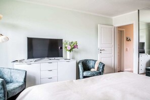 Ein Hotelzimmer mit Bett, Schreibtisch, Flachbildfernseher, zwei Stühlen, einer Tür und einem Spiegel.