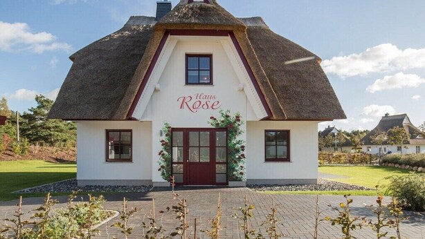 Ein traditionelles Gebäude mit einem Reetdach, mit einem Schild mit der Aufschrift 'Haus Rose' und einem kleinen Fenster über dem Eingang.