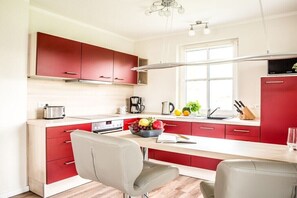 Een moderne keuken met rode kastjes, een wit aanrechtblad en een roestvrijstalen broodrooster.