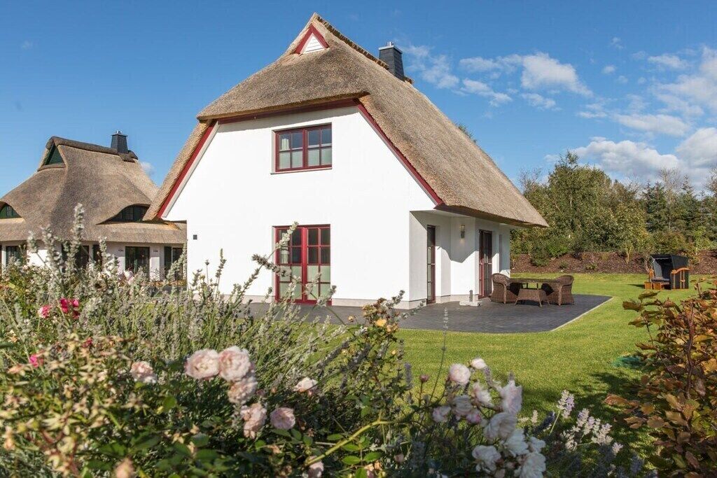 A white house with a thatched roof, a red door, and a small garden with flowers.