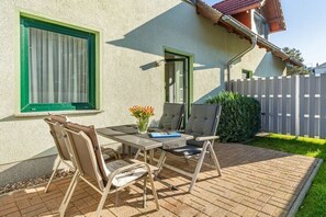 Un pati amb una taula i cadires, un jardí petit i una casa amb marc de finestra verd.